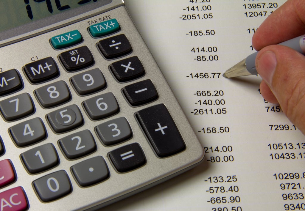 A close up of a calculator that is laying on top of a financial sheet where a hand is seen holding a pen.