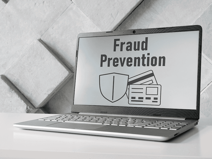 A laptop on a white table displays the words "Fraud Prevention" with images of a shield and payment cards on the screen.