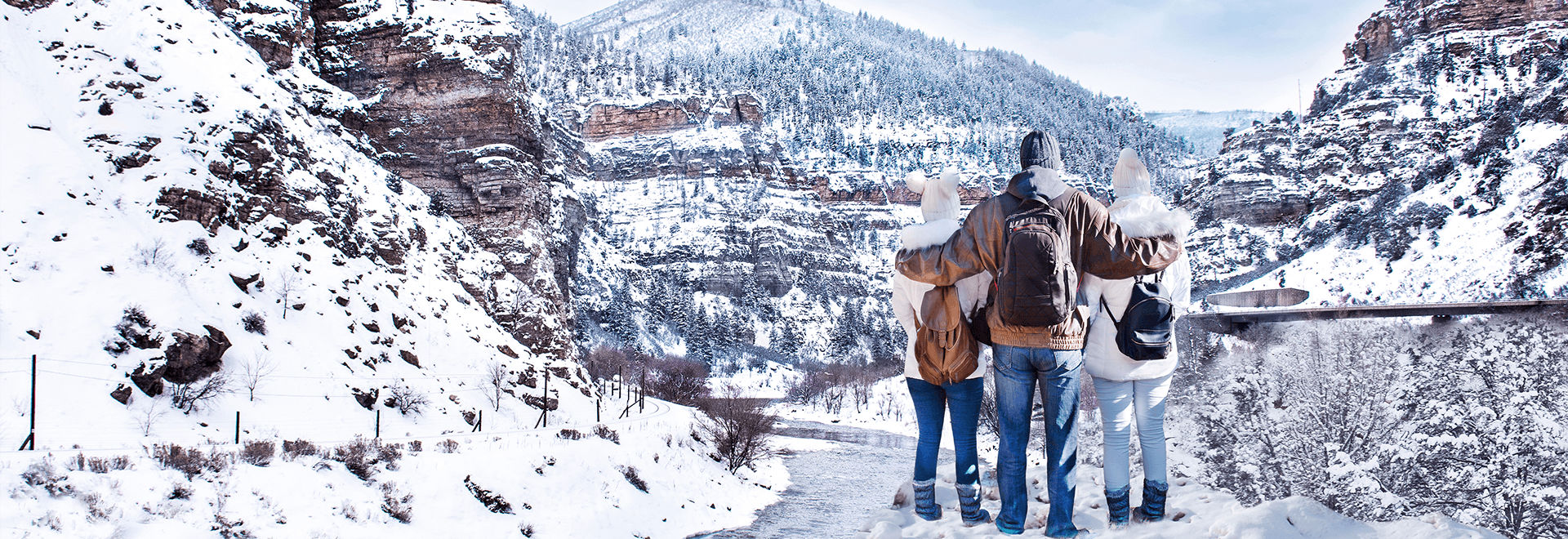 Colorful autumn trees and rustic wooden cabins line the shore of a calm lake, set against a backdrop of forested mountains.