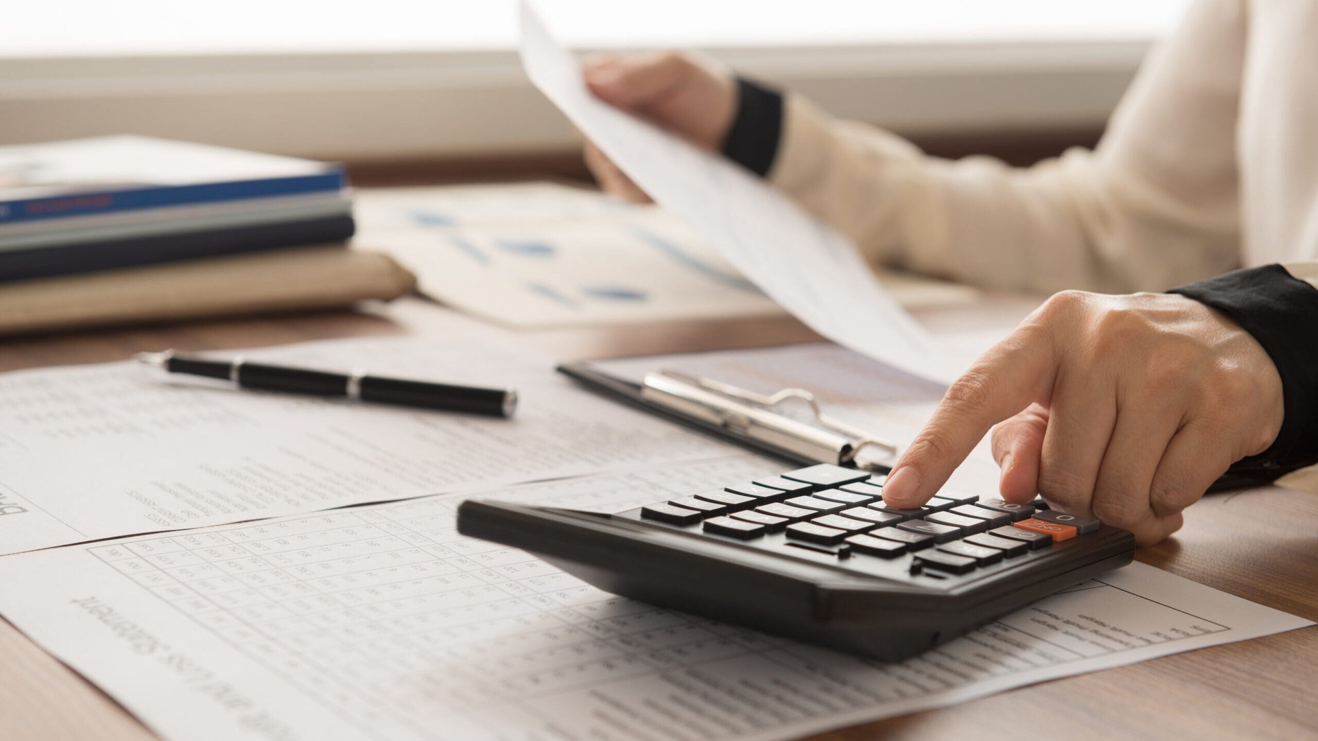 a close-up shot of a person holding papers and using a calculator