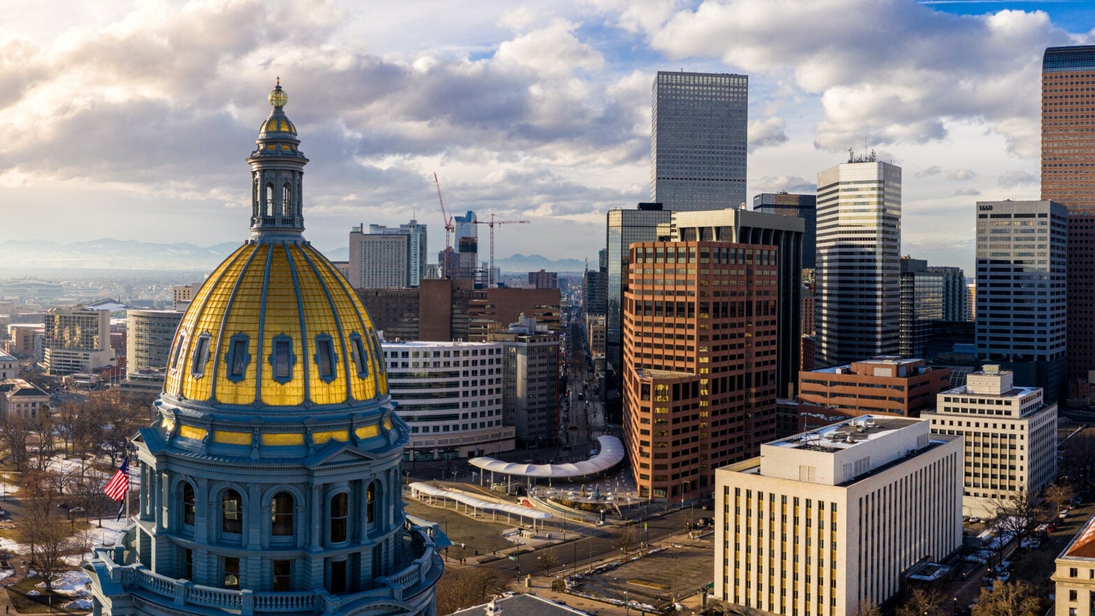 The gold dome of the Colorado State Capitol in the foreground with the Denver skyline behind it