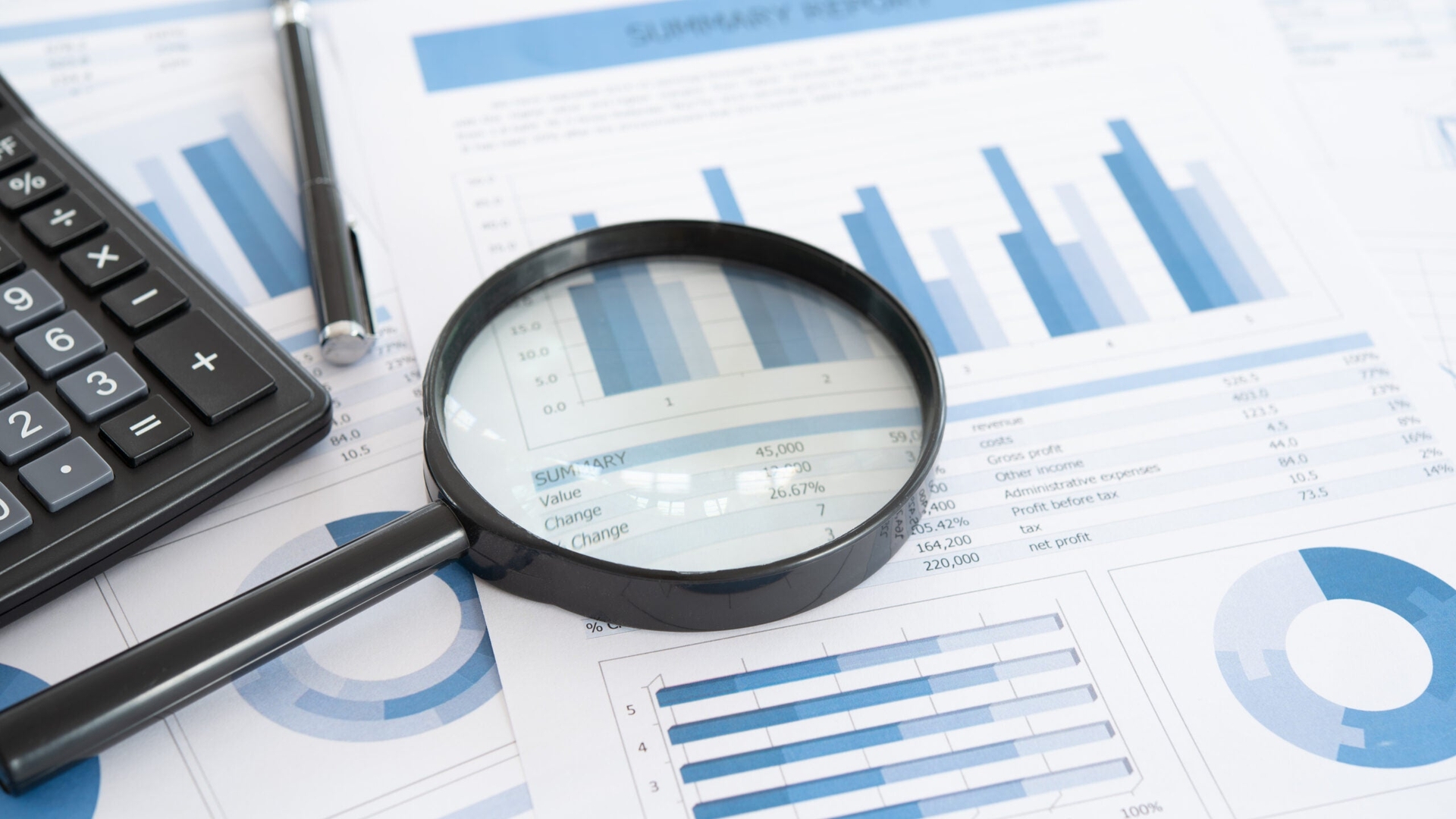A magnifying glass and calculator sit atop a pile of financial papers