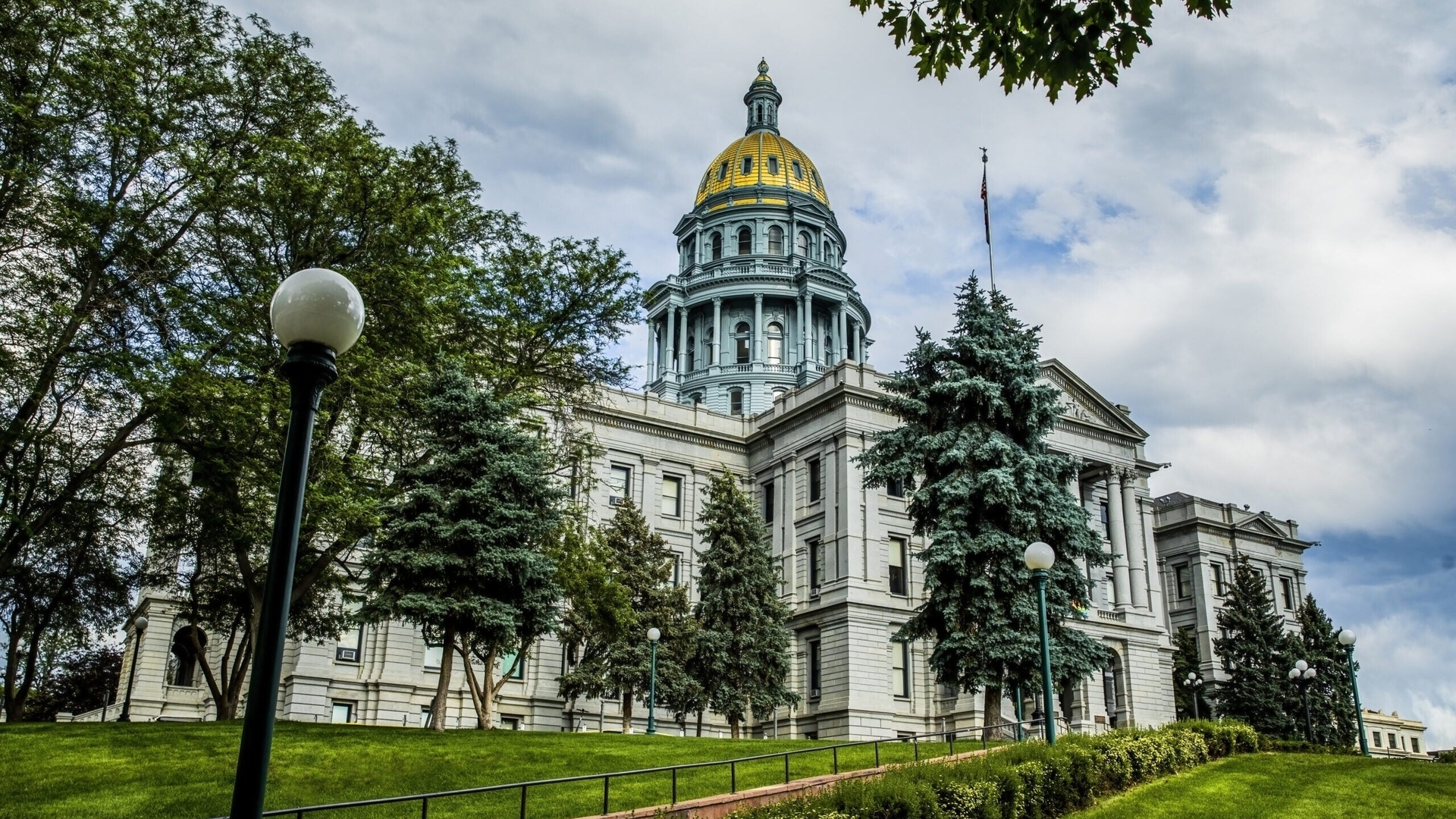 A view of the Colorado State Capitol Building framed by green trees on a mostly cloudy day.