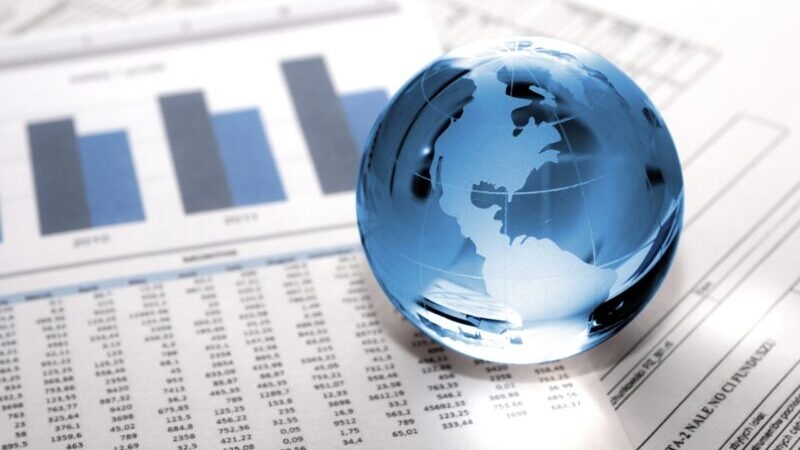 A transparent blue globe sits on financial documents with charts and graphs, representing global finance data.