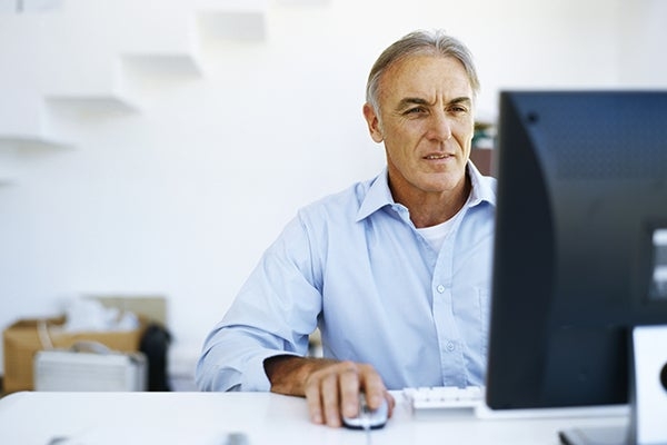 Senior man in a light blue shirt using a desktop computer in a bright room.