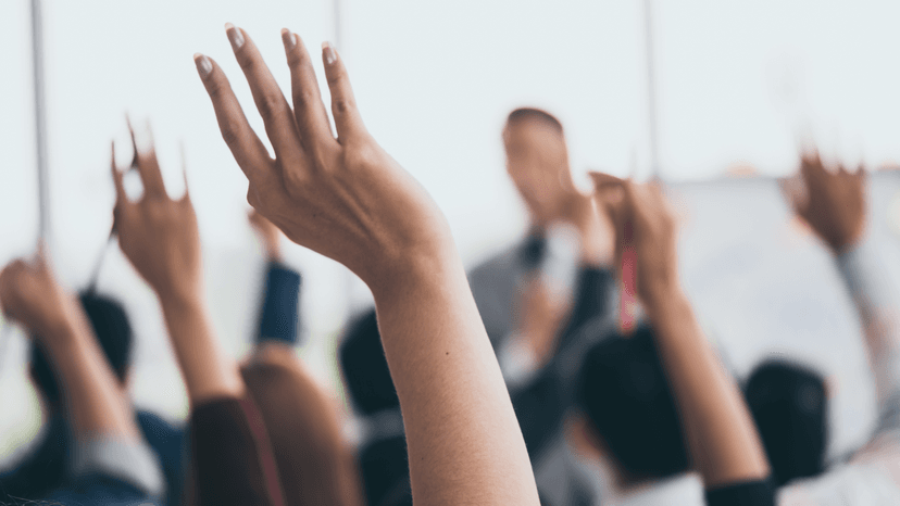 A group of people with raised hands in front of a man speaking.